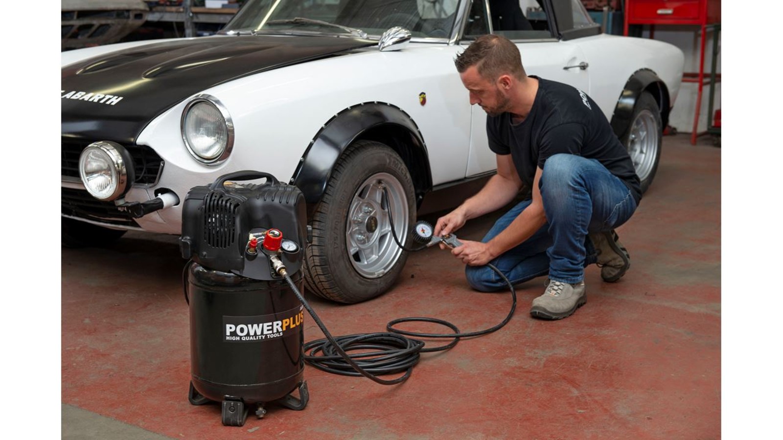 Pildil on mees, kes kasutab Powerplus POWX1731 õlivaba kompressorit, et täita auto rehvi õhuga.